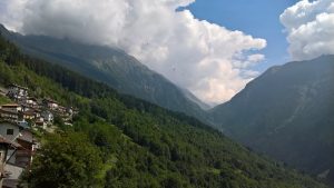 La Casa delle Streghe nestled in lush green Italian Alps landscape with dramatic clouds.