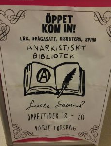 Sign for Anarkistiska Biblioteket Lucia Saornil, reading "Open, Come In! Read, Question, Discuss, Spread.