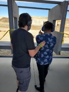 Latino Rifle Association: Person learns to shoot with instructor at outdoor range.