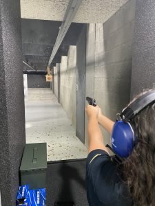 Shooting range: person firing a handgun, ear protection, ammo box. Latino Rifle Association.
