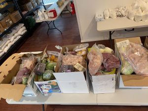 Boxes of food at K'É Infoshop, including produce, meat, and packaged goods ready for distribution.