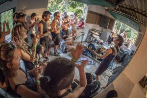 Band Semente Negra performs live for a crowd in an intimate, indoor setting with a fisheye lens view.