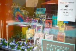 Bookstore window display featuring titles on social justice. "Masks are required.