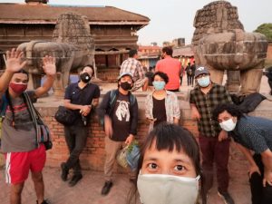 Group wearing masks at The Infoshop Nepal, standing near stone lion statues.
