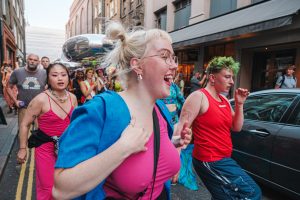 SWARM In The Streets: A vibrant street scene with diverse people celebrating, featuring colorful clothing and expressions of joy.