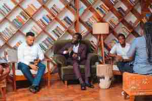 Man speaking at Sankara Pan-African Library event, with audience and bookshelves.